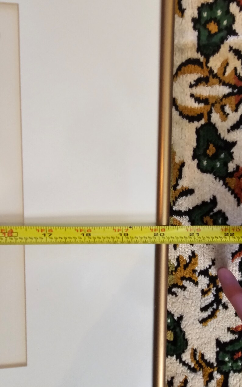May include: A close-up of a white picture frame with a gold metal frame. A yellow measuring tape is placed at the bottom of the frame, showing a measurement of 45.7 cm.