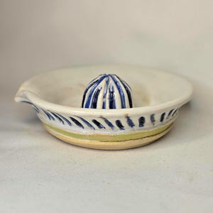 May include: A ceramic citrus juicer with a white bowl and a blue and white reamer. The bowl has a spout and is decorated with blue and green stripes. The reamer is blue and white striped.