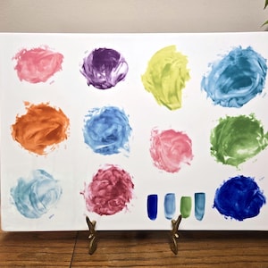 May include: A rectangular white ceramic tray with colorful paint splotches in pink, purple, yellow, blue, orange, and green. The tray is displayed on a wooden surface with a brass stand.