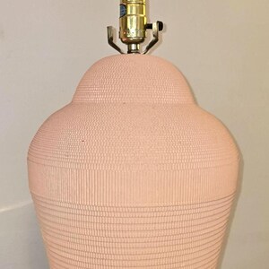 May include: A peach-coloured table lamp with a textured, ribbed surface. The lamp has a bulb and a brass-coloured base. The lamp is on a wooden surface.