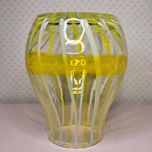 May include: A clear glass vase with yellow and white vertical stripes and a horizontal yellow band. The vase has a flared shape and is likely used for decorative purposes.
