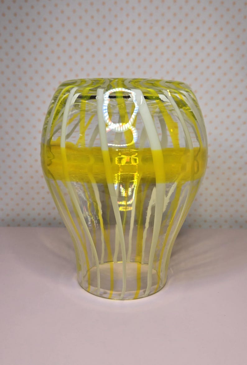 May include: A clear glass vase with yellow and white vertical stripes and a horizontal yellow band. The vase has a flared shape and is likely used for decorative purposes.