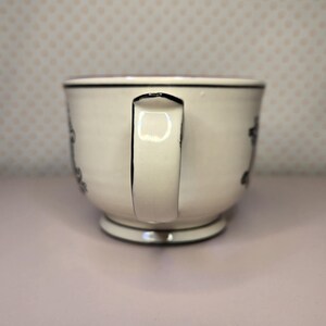 May include: A white ceramic mug with a black handle and the text "But First, Coffee" in a handwritten style. The mug is on a white surface. The mug is 4 inches tall.