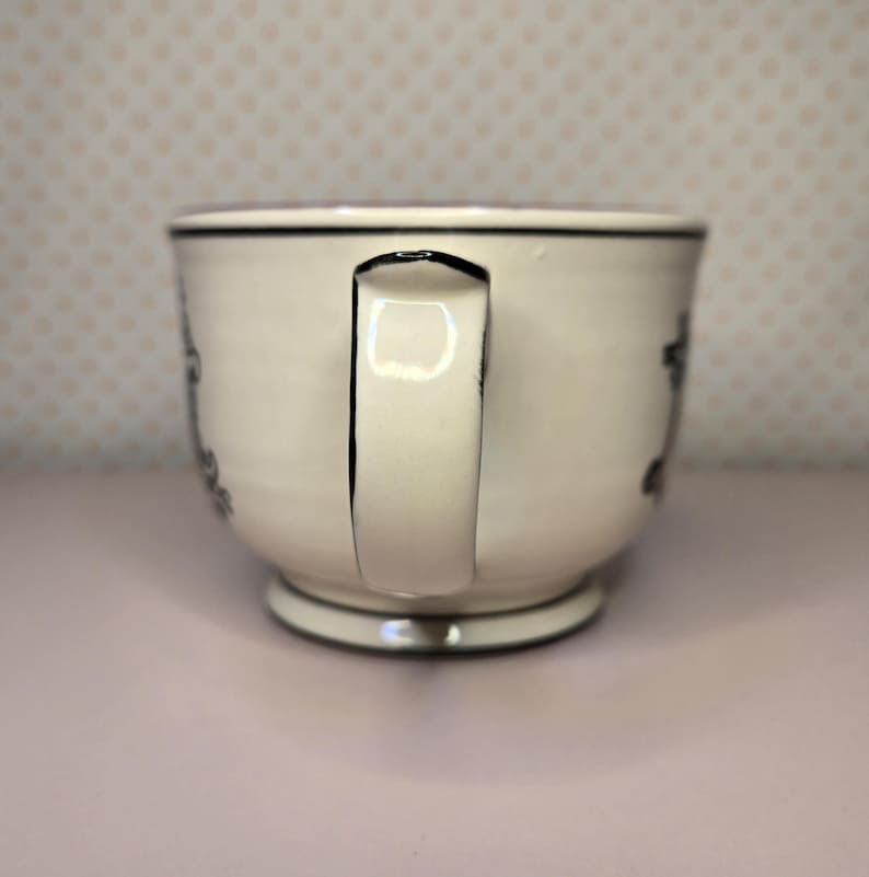 May include: A white ceramic mug with a black handle and the text "But First, Coffee" in a handwritten style. The mug is on a white surface. The mug is 4 inches tall.