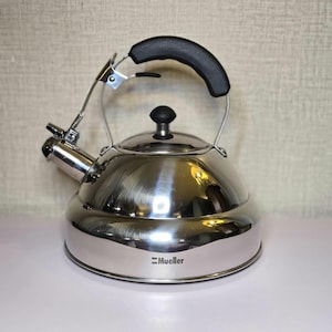 May include: A stainless steel tea kettle with a black handle and spout. The kettle has a shiny, reflective surface and a black knob on the lid. The brand name "Mueller" is printed on the front.