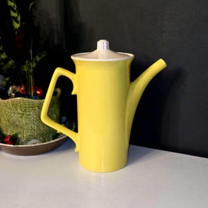May include: A yellow ceramic coffee pot with a white lid and a long spout. The pot has a modern design and is perfect for serving coffee or tea.