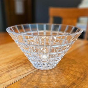 May include: A clear glass bowl with a geometric pattern. The bowl is made of crystal and has a wide, flared rim.