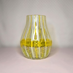 May include: A clear glass vase with vertical yellow and white stripes. The vase has a rounded shape with a wide base and a narrower neck. The interior of the vase is filled with a yellow substance, adding a pop of color.