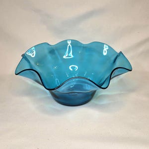 May include: A turquoise glass bowl with a ruffled rim and a black edge. The bowl has a rounded base and a wavy, scalloped edge. The glass is translucent, allowing light to pass through.