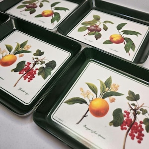 May include: A set of rectangular dark green serving trays featuring white center panels with botanical illustrations of various fruits, including oranges, red currants, and peaches, accompanied by small printed text labels.