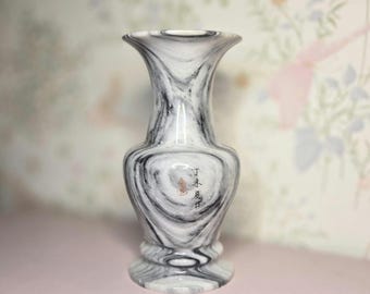 May include: A decorative vase with a swirling black and white pattern. The vase has a flared top and a rounded base. The vase has a small inscription in the center. The vase is made of a glossy material.