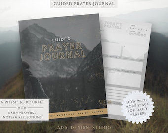 May include: A guided prayer journal with a mountain landscape cover. The journal includes space for daily prayers, notes, and reflections. The cover text reads "Guided Prayer Journal" in gold lettering. The journal is a physical booklet.