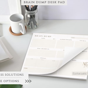 May include: A beige Brain Dump desk pad with sections for to-do lists, notes, and contact information. The pad has a customizable text option and is designed for business solutions. A white mug, pencils, and a keyboard are also visible.