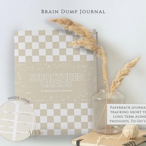 Könnte beinhalten: Ein kariertes Notizbuch in Beige und Weiß mit dem Titel "Brain Dump Journal" und den Worten "Structured Chaos" auf dem Cover. Das Notizbuch wird mit getrockneten Pflanzen in einer Glasvase und einem kleinen Notizbuch präsentiert. Das Notizbuch dient zum Verfolgen von Agenden, Gedanken und To-Dos.