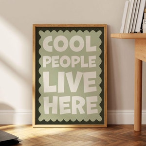 May include: A framed print with a green background and white text that reads "Cool People Live Here". The frame is made of wood and has a light brown finish.