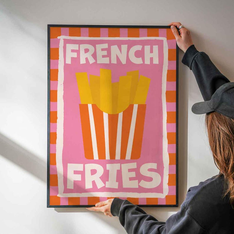 May include: A framed poster with the words "FRENCH FRIES" in white block letters. The poster features a pink background with a graphic of yellow fries in a red and white striped container. The border is orange and white checkered.