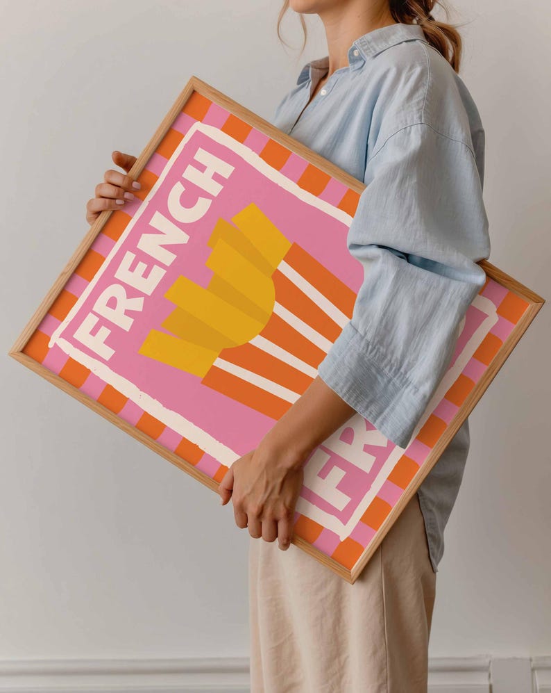 May include: A framed art print featuring a pink background with the words "FRENCH FRY" in white. The artwork depicts a stylized image of golden french fries. The frame is a light wood color with orange and white stripes.