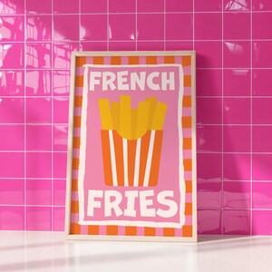 May include: A framed print featuring a pink background with the words "FRENCH FRIES" in white. The image includes a graphic of a container of yellow french fries with orange and white stripes.