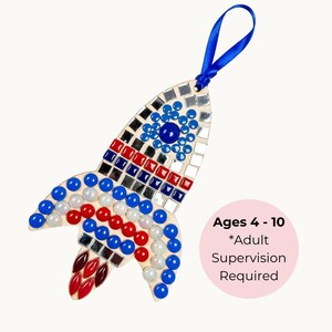 May include: A wooden rocket-shaped craft kit decorated with blue, red, white, and mirrored mosaic tiles. It has a blue ribbon for hanging. The text on the image says "Ages 4-10 *Adult Supervision Required."
