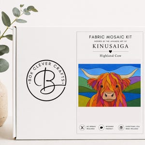 Op de afbeelding: Een witte rechthoekige doos voor een stoffen mozaïekset met het Box Clever Crafts logo en de tekst Fabric Mosaic Kit, Inspired by the Japanese Art of Kinusaiga, Highland Cow. De doos toont een kleurrijke illustratie van een koe.