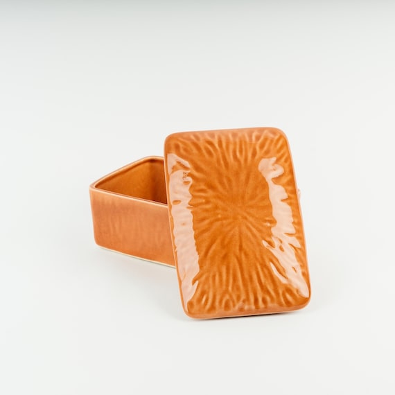 A richly glazed burnt-orange lidded butter dish that turns a mundane counter staple into a farmhouse statement piece.