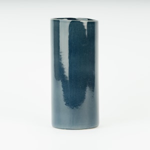 May include: A tall, cylindrical vase with a glossy, dark teal glaze. The ceramic vase has a slightly irregular rim and a smooth, reflective surface. The vase is a solid colour and stands upright against a white background.