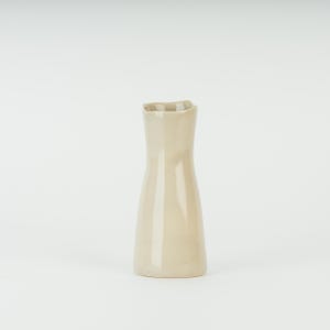 May include: A small, cream-colored ceramic vase with a slightly irregular, wavy rim.