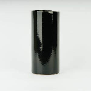 May include: A black ceramic vase with a smooth, glossy finish. The vase is cylindrical in shape and has a slightly irregular opening at the top.
