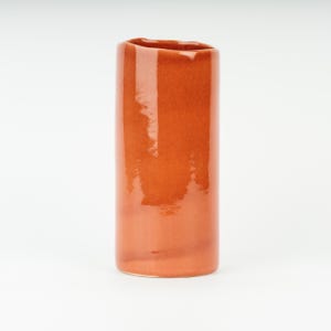 May include: A terracotta-colored ceramic vase with a slightly uneven, rounded top and a glossy finish.
