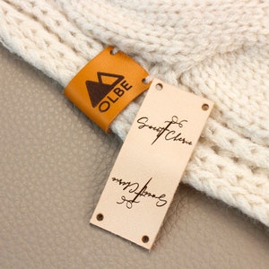 May include: Two leather labels with brown text. The first label is orange and has a mountain logo and the text "OLBE". The second label is beige and has the text "Sweet Cherie" and "Made with Love".