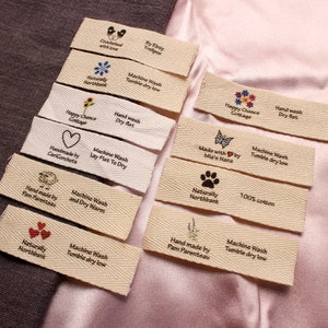 May include: A collection of 10 fabric labels with various designs and text. The labels are made of natural cotton and have a woven texture. The text on the labels includes "Machine Wash", "Tumble Dry Low", "Hand Wash", "Dry Flat", "Naturally Northbank", "100% Cotton", "Handmade by", "Happy Chance Cottage", "Crocheted with love", "By Elray Trollpor", "Made with by Mia's Nana".