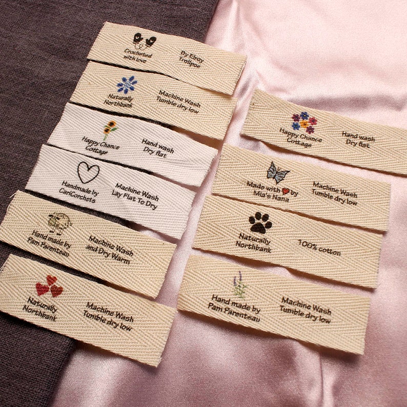 May include: A collection of 10 fabric labels with various designs and text. The labels are made of natural cotton and have a woven texture. The text on the labels includes "Machine Wash", "Tumble Dry Low", "Hand Wash", "Dry Flat", "Naturally Northbank", "100% Cotton", "Handmade by", "Happy Chance Cottage", "Crocheted with love", "By Elray Trollpor", "Made with by Mia's Nana".