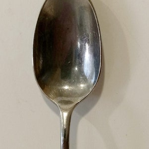 May include: A silver spoon with an ornate, gold-toned handle. The handle is decorated with a swirling, floral design.