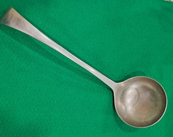 May include: A silver ladle with a long handle. The ladle is on a green surface.