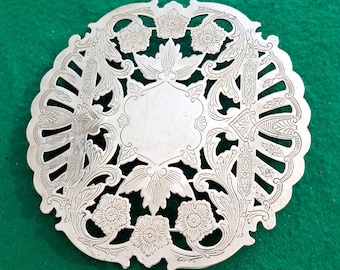 May include: Silver filigree coaster with a floral design. The coaster has a circular shape and is made of metal.
