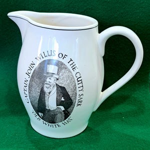 May include: White ceramic pitcher with a black and white illustration of Captain John Willis of the Cutty Sark. The illustration shows a man in a top hat and a long coat with the text "Old White Hat".