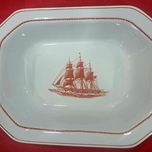 May include: A white ceramic serving dish with a brown rope design around the edge. The dish features a brown illustration of a sailing ship in the center.