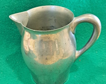 May include: A silver pitcher with a rounded body and a handle. The pitcher is made of metal and has a shiny finish.