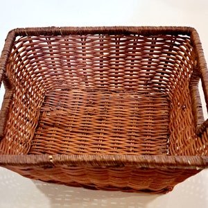 May include: A brown wicker basket with a rectangular shape and two handles on the sides. The basket is made of woven wicker and has a natural brown color.