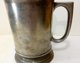 May include: A pewter tankard with a rounded body and a single handle. The tankard has a slightly flared lip and a base with a raised ring.