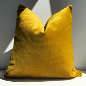 May include: A mustard yellow velvet pillow with a soft, plush texture. The pillow is square shaped and has a simple design.