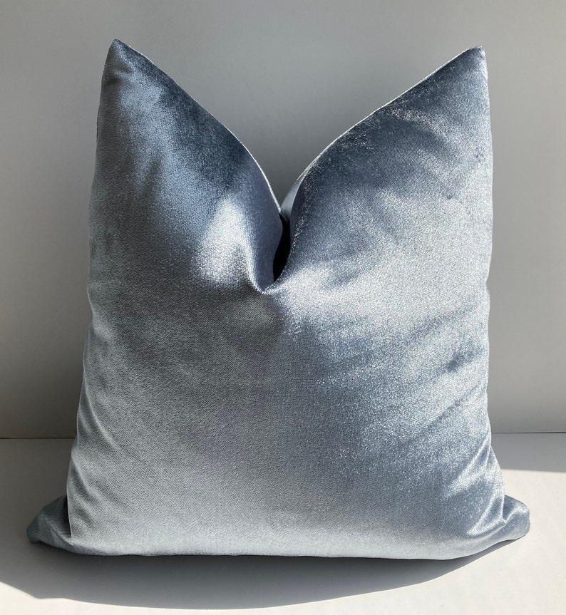 May include: A soft, light blue velvet pillow cover. The pillow is square and has a smooth, luxurious texture.