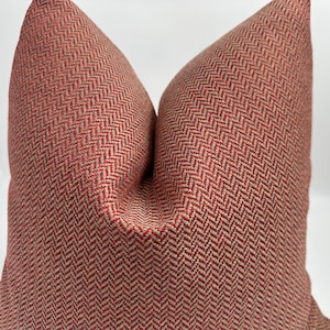 May include: Red and beige herringbone patterned throw pillow. The pillow is made of a soft, textured fabric.