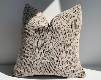May include: A decorative cushion with a black and beige abstract pattern. The cushion is made of a soft, textured fabric.