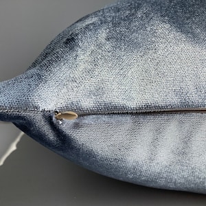 May include: A close-up of a blue velvet pillow with a zipper closure. The pillow is soft and plush, and the zipper is hidden.