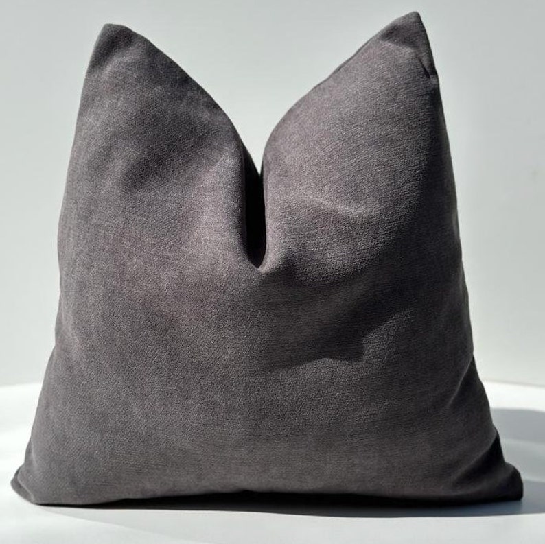 May include: A dark gray throw pillow with a textured fabric. The pillow is square shaped and has a simple design.