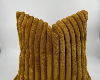 May include: Mustard-colored decorative pillow with a corduroy texture. The pillow has a rectangular shape and a soft, plush appearance. The vertical ridges create a textured surface, adding visual interest to the home decor item.