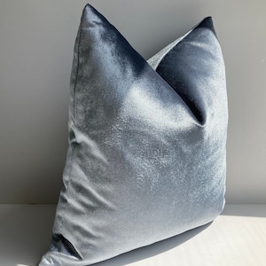May include: A light blue velvet pillow with a soft, plush texture. The pillow is shown on a white surface.