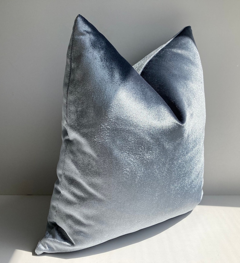 May include: A light blue velvet pillow with a soft, plush texture. The pillow is shown on a white surface.