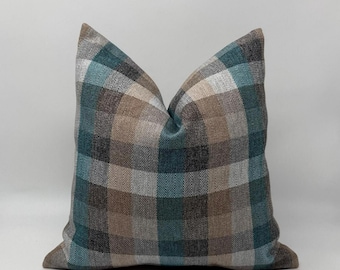 May include: Square decorative pillow with a plaid pattern in shades of teal, brown, beige, and gray. The pillow has a soft, textured appearance and is likely made of fabric. The pillow is a home decor item.